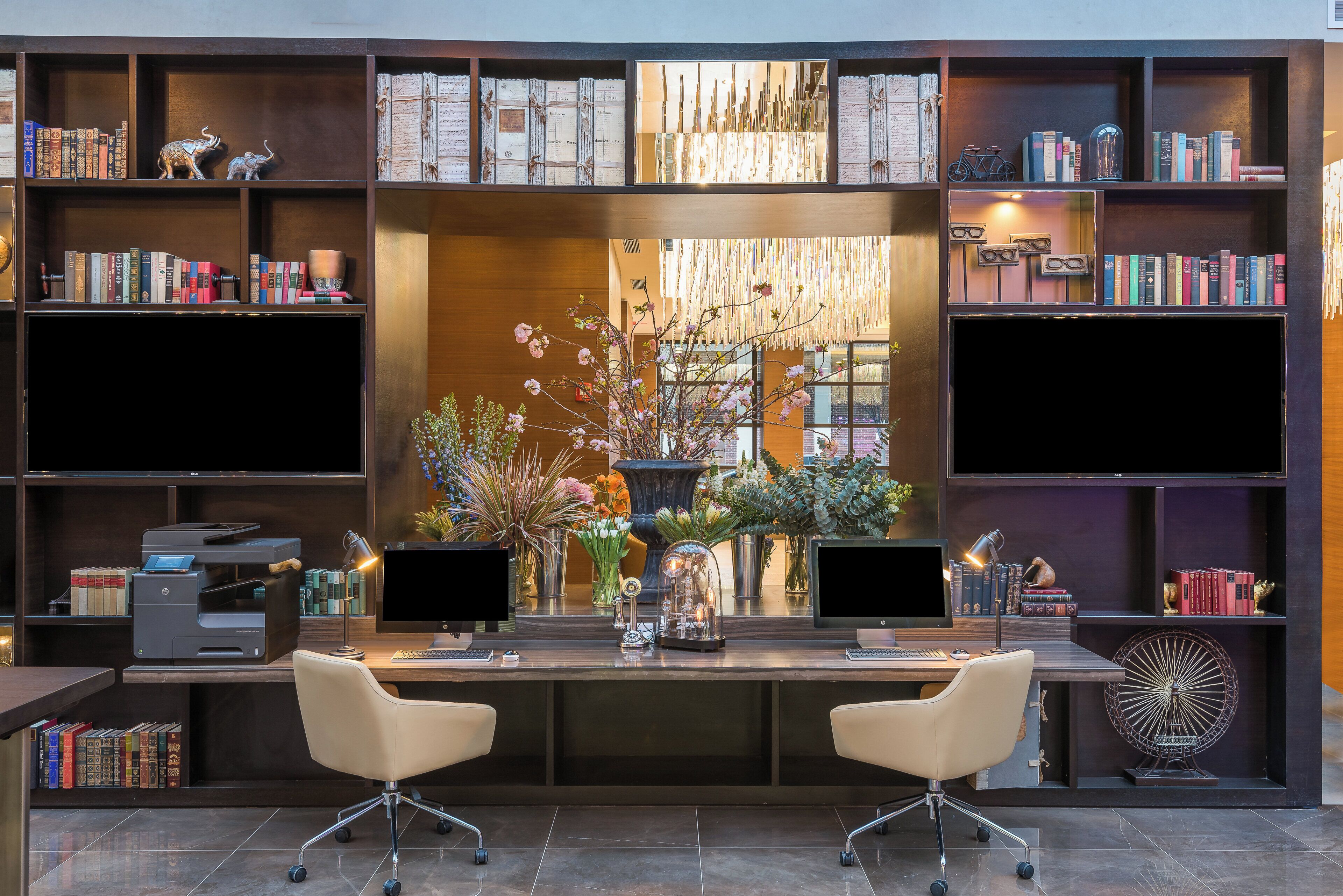 A modern office space with two desks, chairs, and a large bookshelf filled with books.