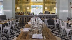 Un restaurant avec une longue table en bois dressée pour le repas, des chaises blanches et un bar situé au fond de la salle.