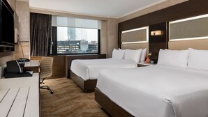 Une chambre d’hôtel avec deux lits, un bureau avec une chaise, une télévision et une grande fenêtre donnant sur la ville.
