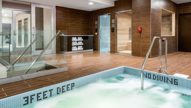 Un espace piscine intérieur moderne, avec un panneau indiquant « INTERDIT DE PLONGER », des rampes en verre et un indicateur de profondeur indiquant « 1 MÈTRE DE PROFONDEUR ».