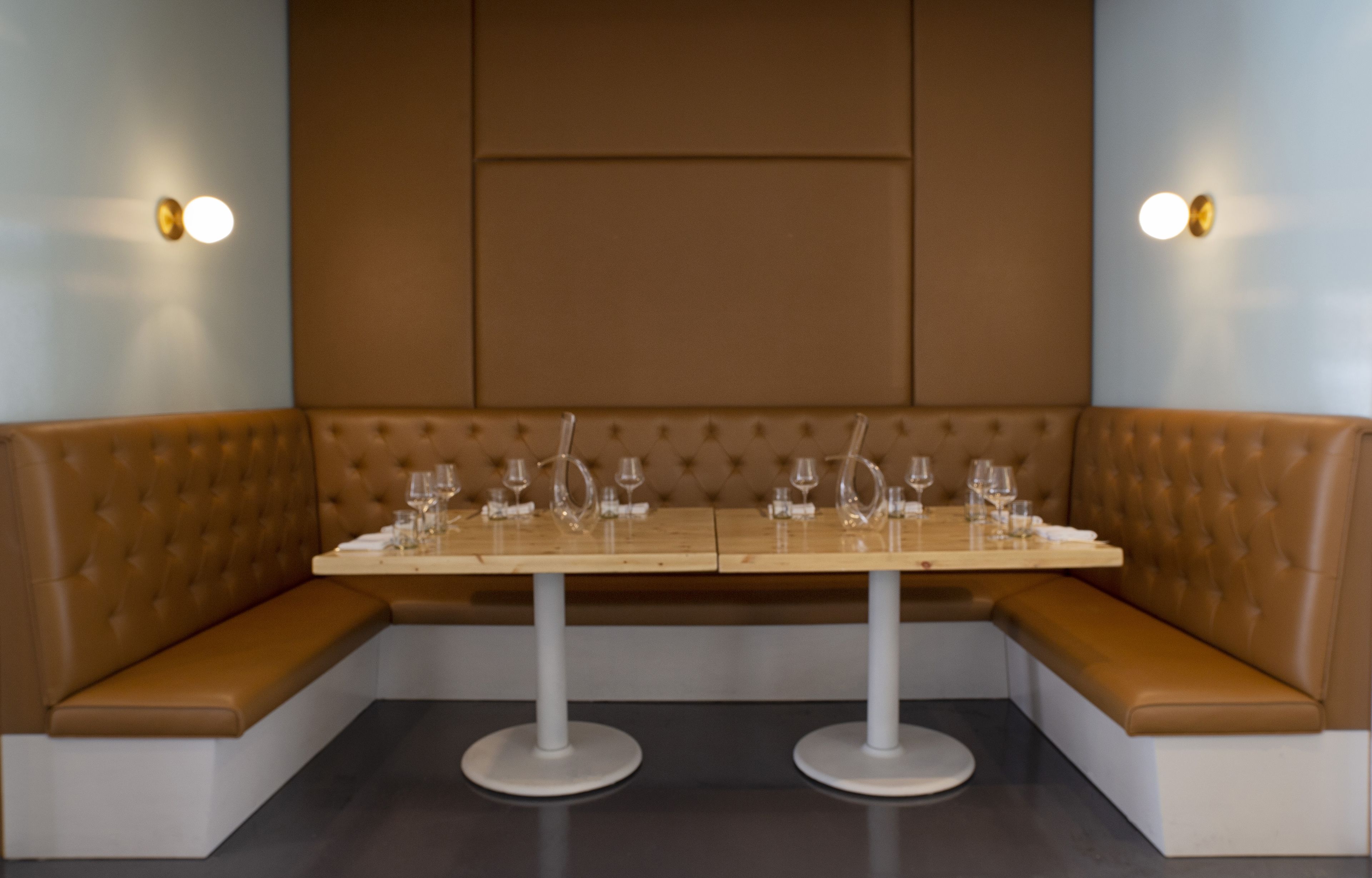 A corner booth with a wooden table set for dining, cushioned seating, and wall-mounted lighting.
