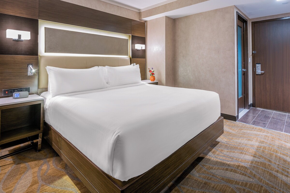 Una habitación de hotel con una cama grande, mesitas de noche, una lámpara de pared y una puerta.