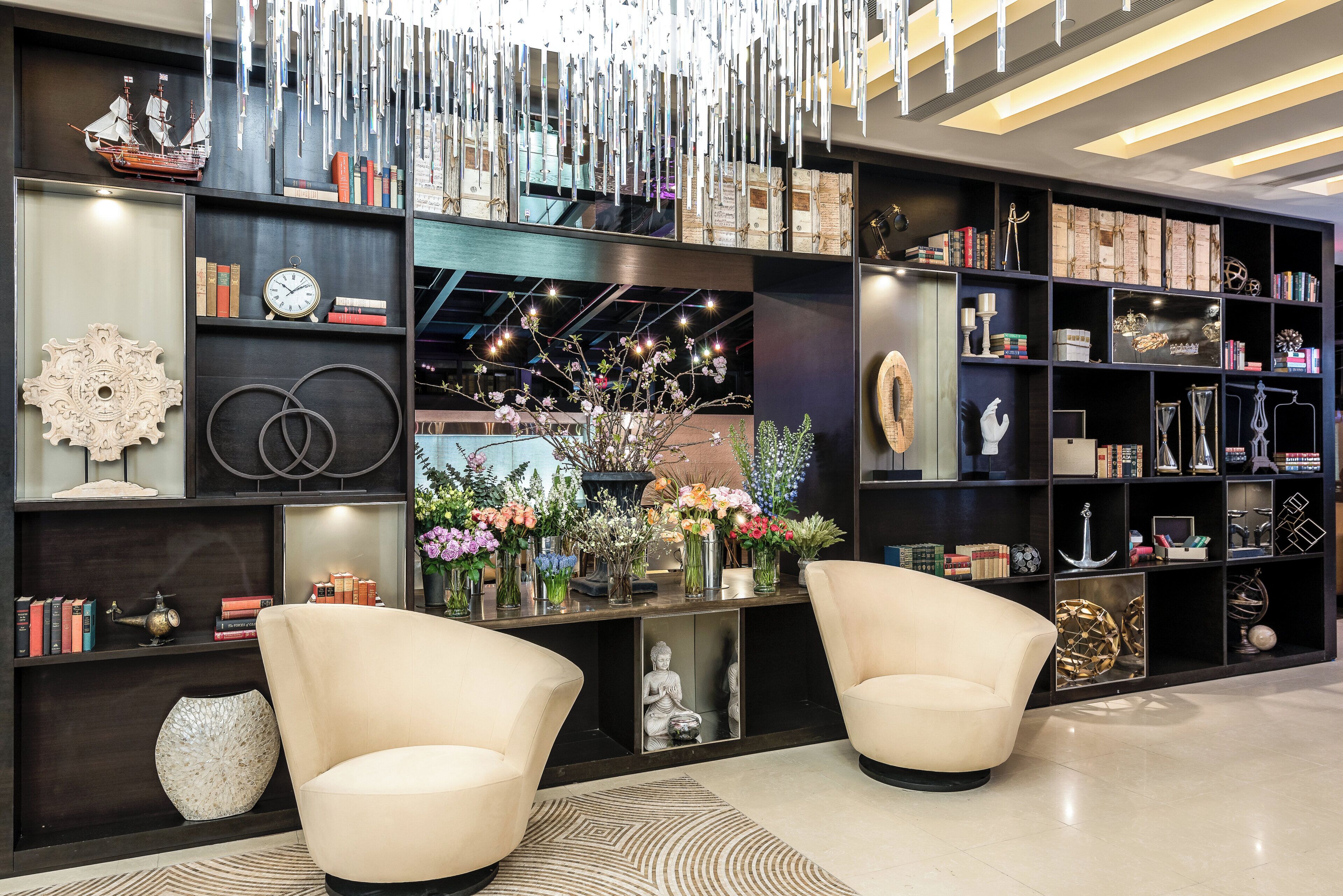 A modern interior with two armchairs, a bookshelf with various items, and a decorative hanging installation.