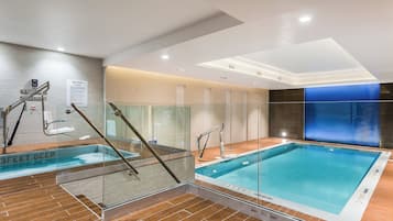 An indoor swimming pool with glass railings, a wooden floor, and a spa area with a sign indicating spa rules.