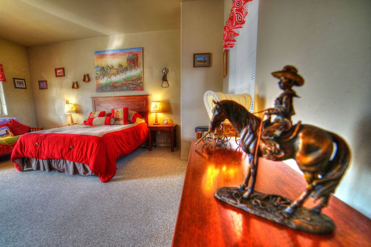 A hotel room with a bed, a nightstand, a lamp, a wall clock, and a decorative horse statue.