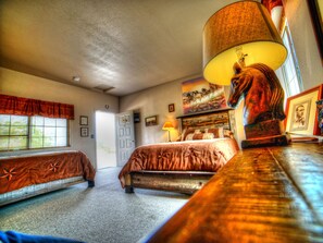 A bedroom with two beds, a large window with blinds, a door, and a lamp on a nightstand.