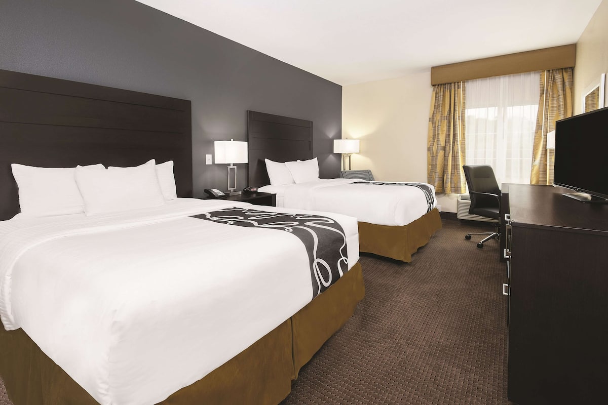 A hotel room with two beds, a desk, a TV, and a chair.