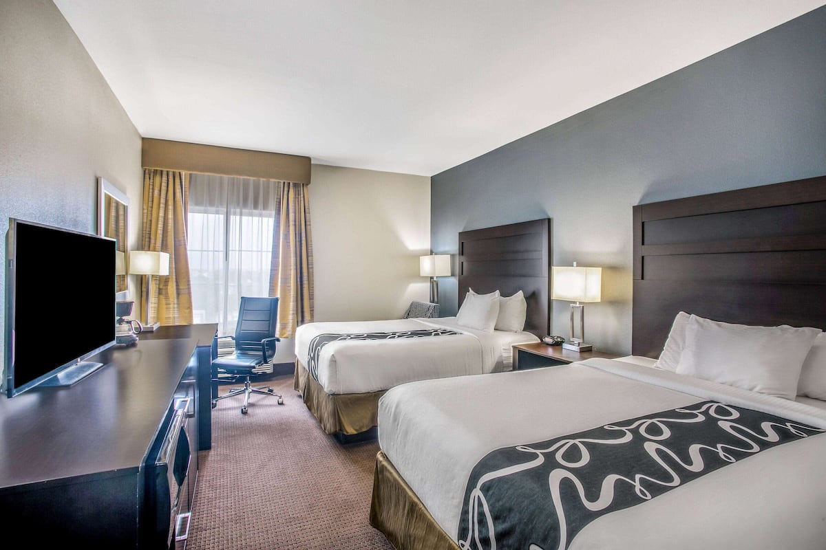 A hotel room with two beds, a desk with a TV, and a window with curtains.