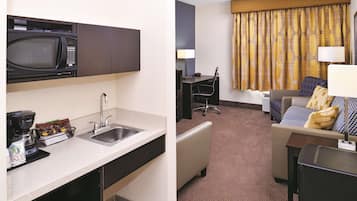 Habitación de hotel con kitchenette, que incluye microondas, fregadero y cafetera. Hay un escritorio con silla y un sofá con cojín estampado.