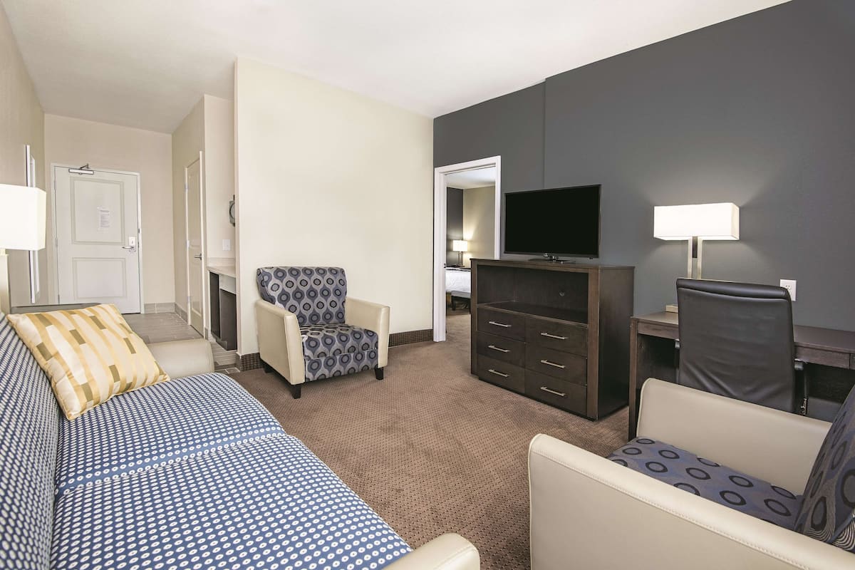 A hotel room with a bed, two armchairs, a TV, a dresser, and a lamp.