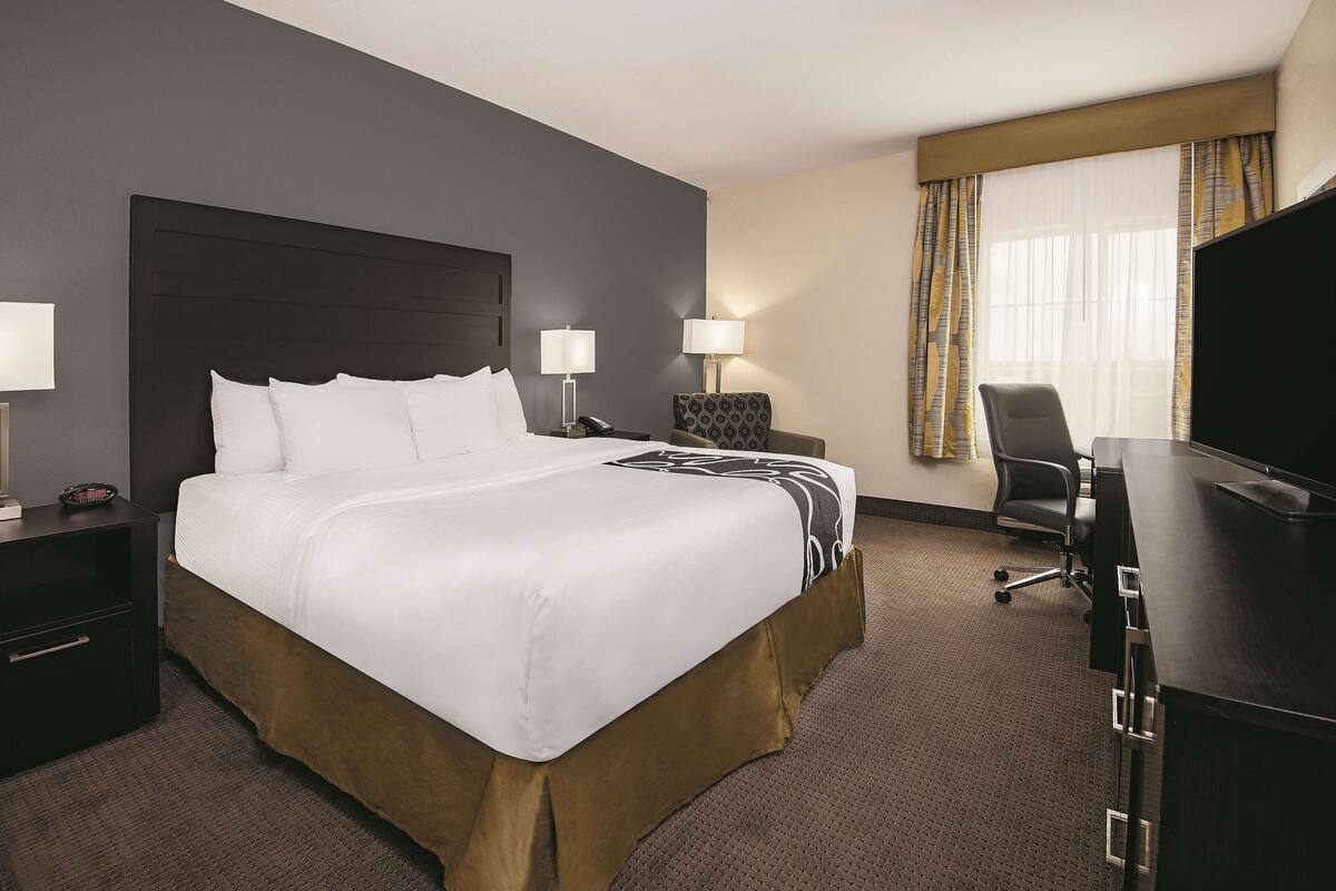 A hotel room with a large bed, two bedside tables with lamps, a desk with a chair, and a television.