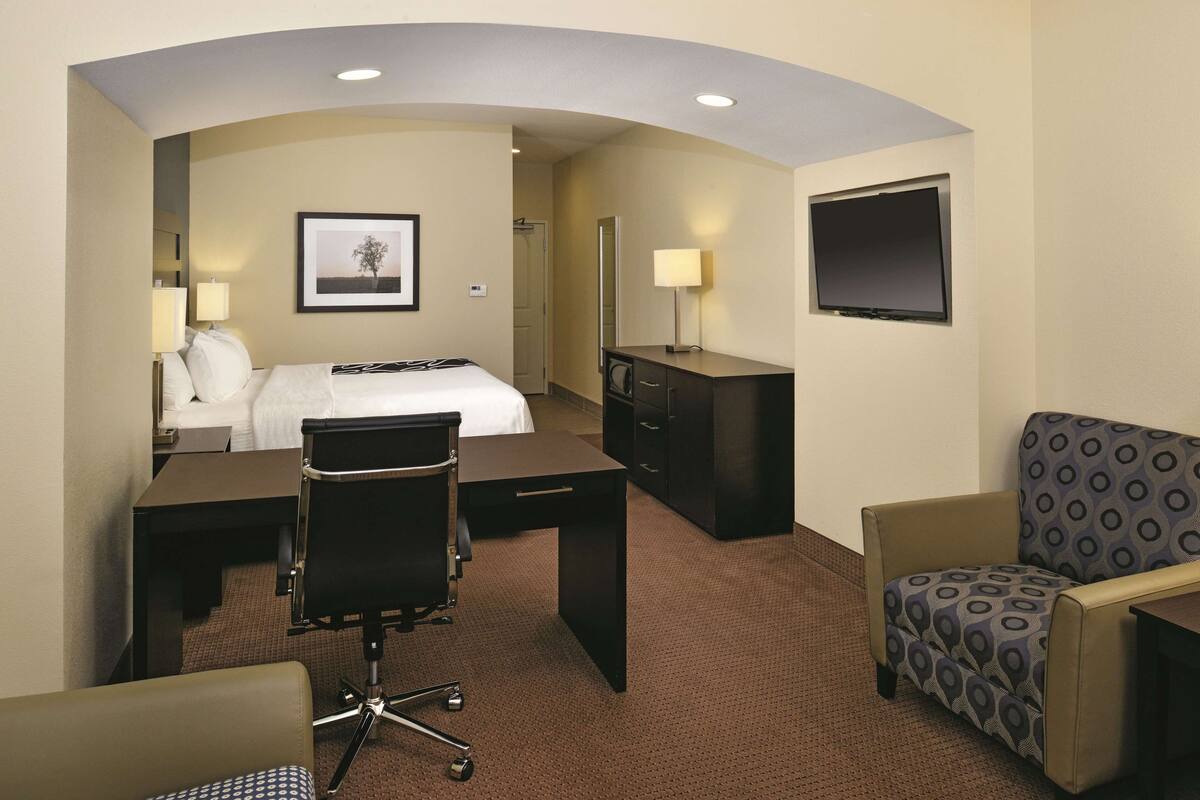 A hotel room with a bed, desk, office chair, and a patterned armchair.