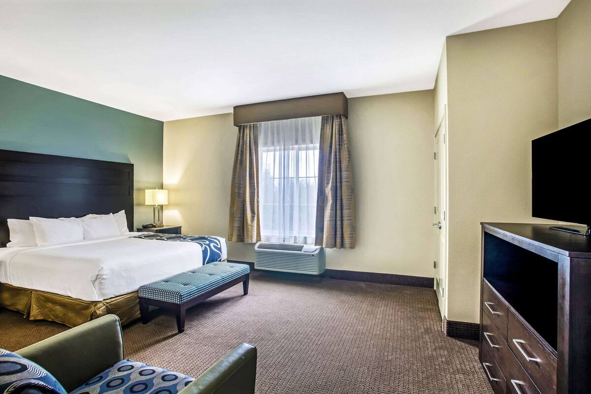 A hotel room with a bed, a desk, a chair, a television, and an air conditioning unit.