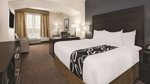 Quarto de hotel com uma cama grande, uma escrivaninha, uma cadeira, televisão e janela com cortinas.
