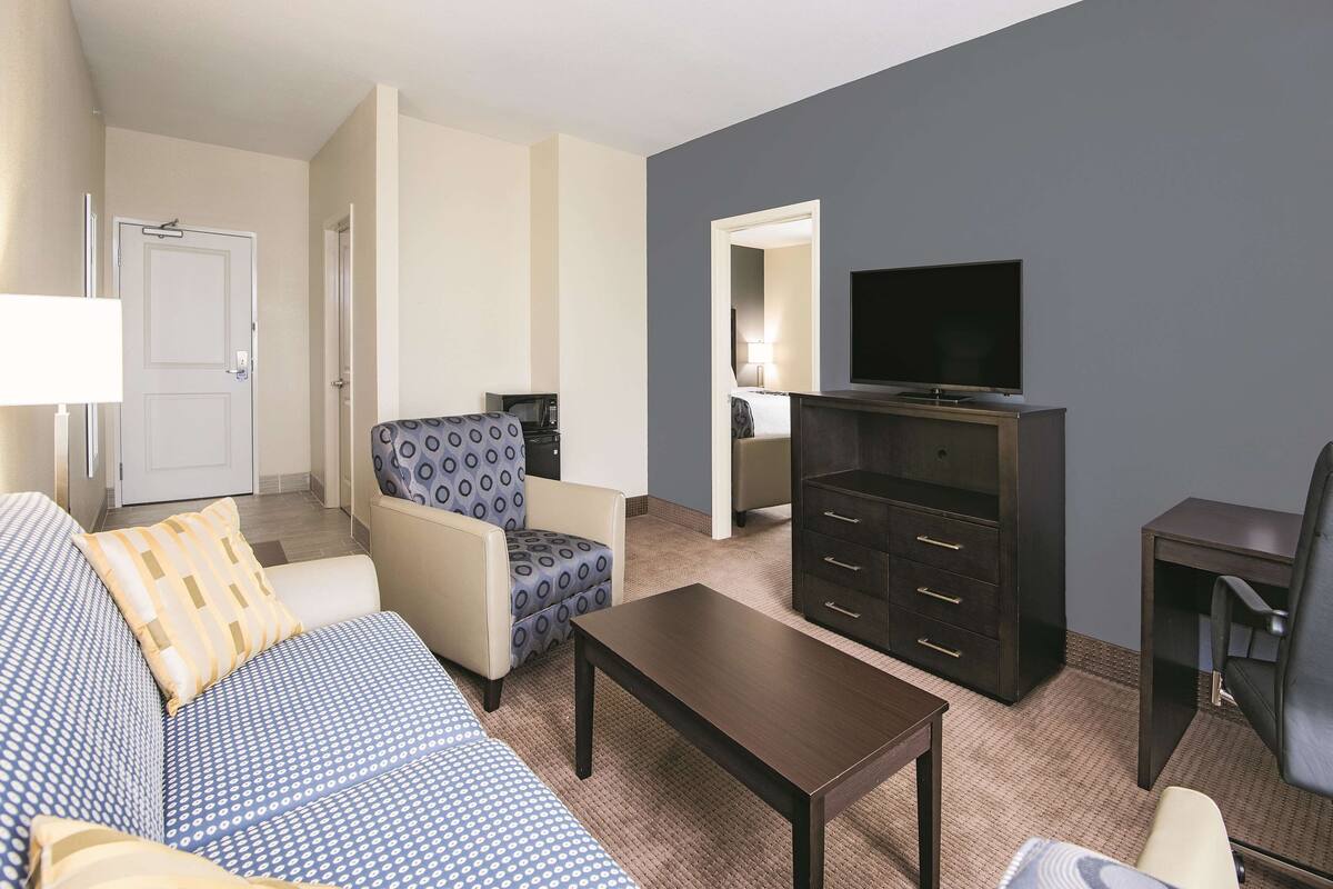 A hotel room with a sofa, armchair, TV, dresser, and a small table.