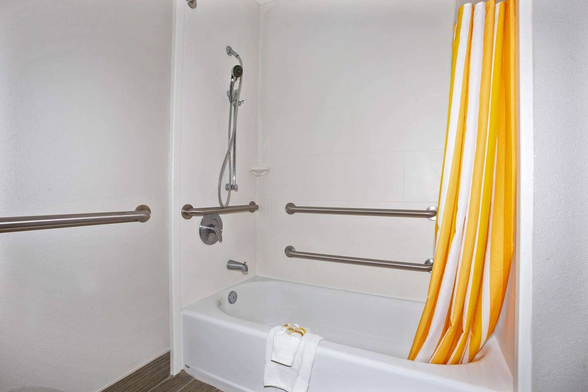 A bathroom with a white bathtub, grab bars, a showerhead, and a yellow-striped shower curtain.