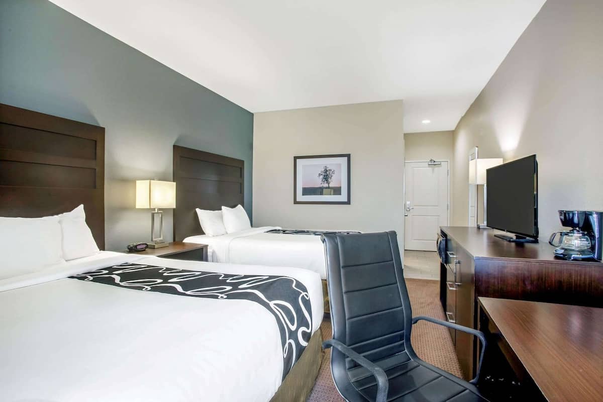 A hotel room with two beds, a desk, a chair, a television, and a coffee maker.
