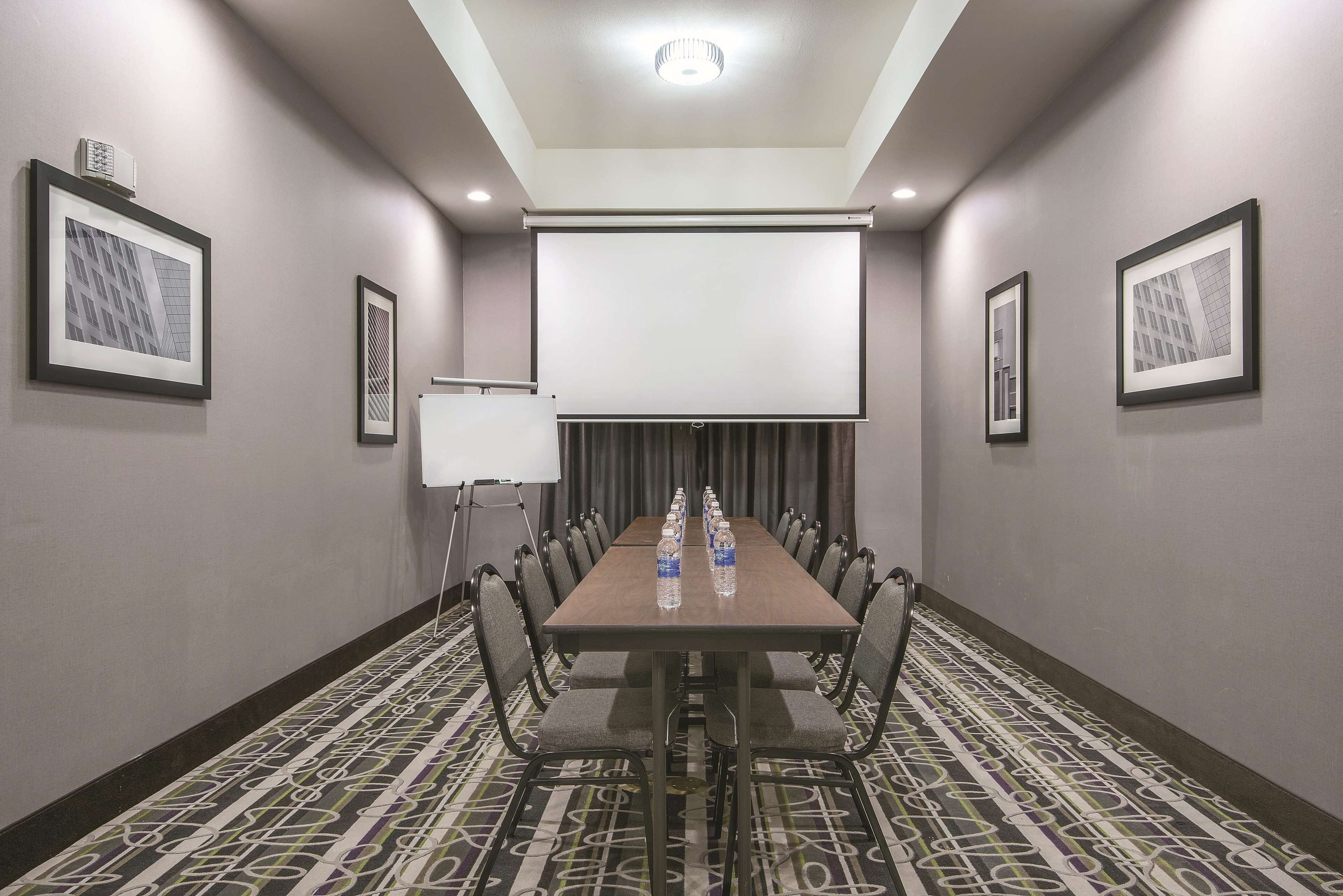A conference room with a long table, chairs, a projector screen, and framed pictures on the walls.