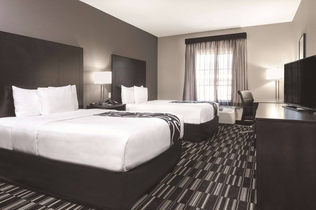 Ein Hotelzimmer mit zwei Betten, einem Schreibtisch, einem Stuhl, einem Fernseher und einem Fenster mit Vorhängen.