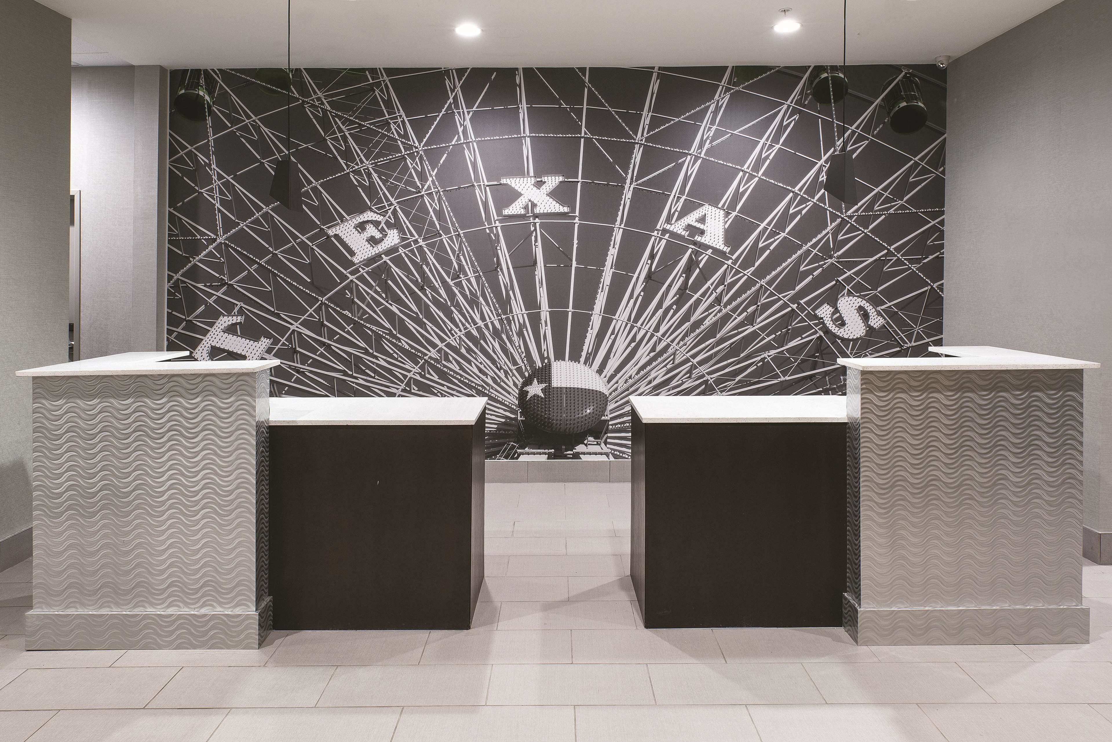 A reception area with a modern design, featuring a large wall with the word "TEXAS" and a decorative sphere in the center. There are two reception desks with patterned designs.