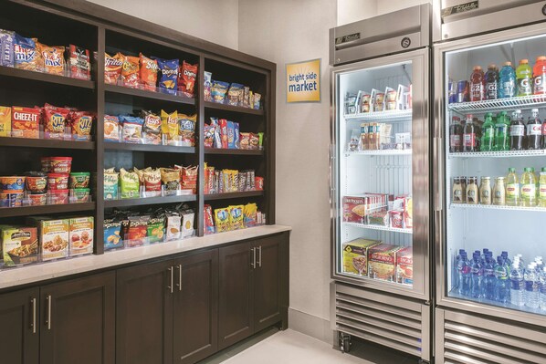 Una tienda de comestibles con estantes llenos de refrigerios y una sección refrigerada con agua embotellada.