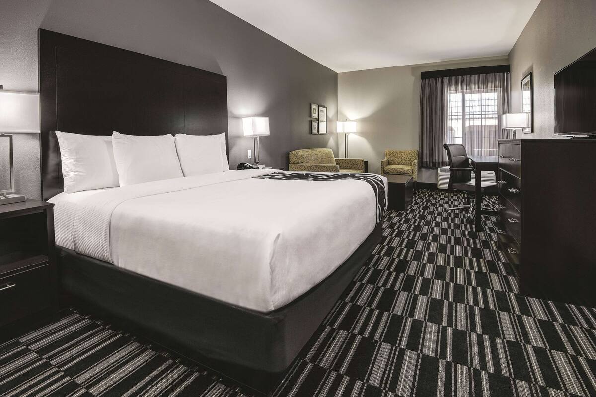 Ein Hotelzimmer mit einem großen Bett, zwei Sesseln, einem Schreibtisch und einem Fernseher.