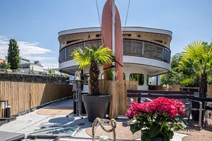 A modern building with a curved facade, a large potted plant, and a surfboard mounted on a pole. - Schiffsherberge Pöppelmann (Dresden)