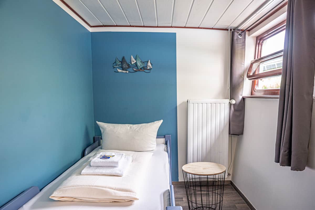 A small, single-bed room with a blue accent wall, a small round table, and a window with curtains.