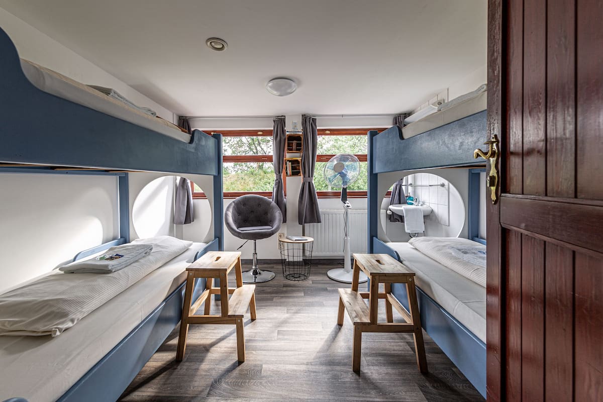 A compact cabin with two bunk beds, a small round table, a chair, and a window with curtains.