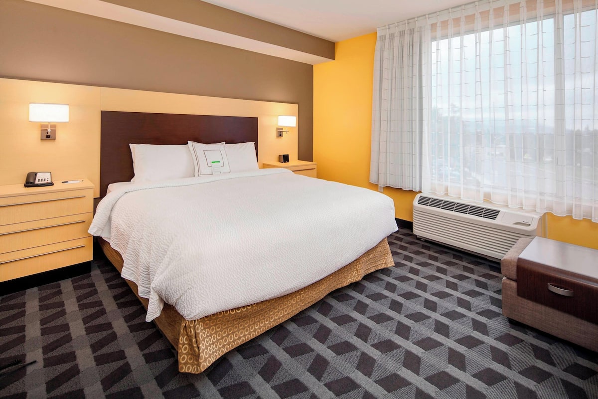 A hotel room with a large bed, bedside tables, a heater, and a window with curtains.