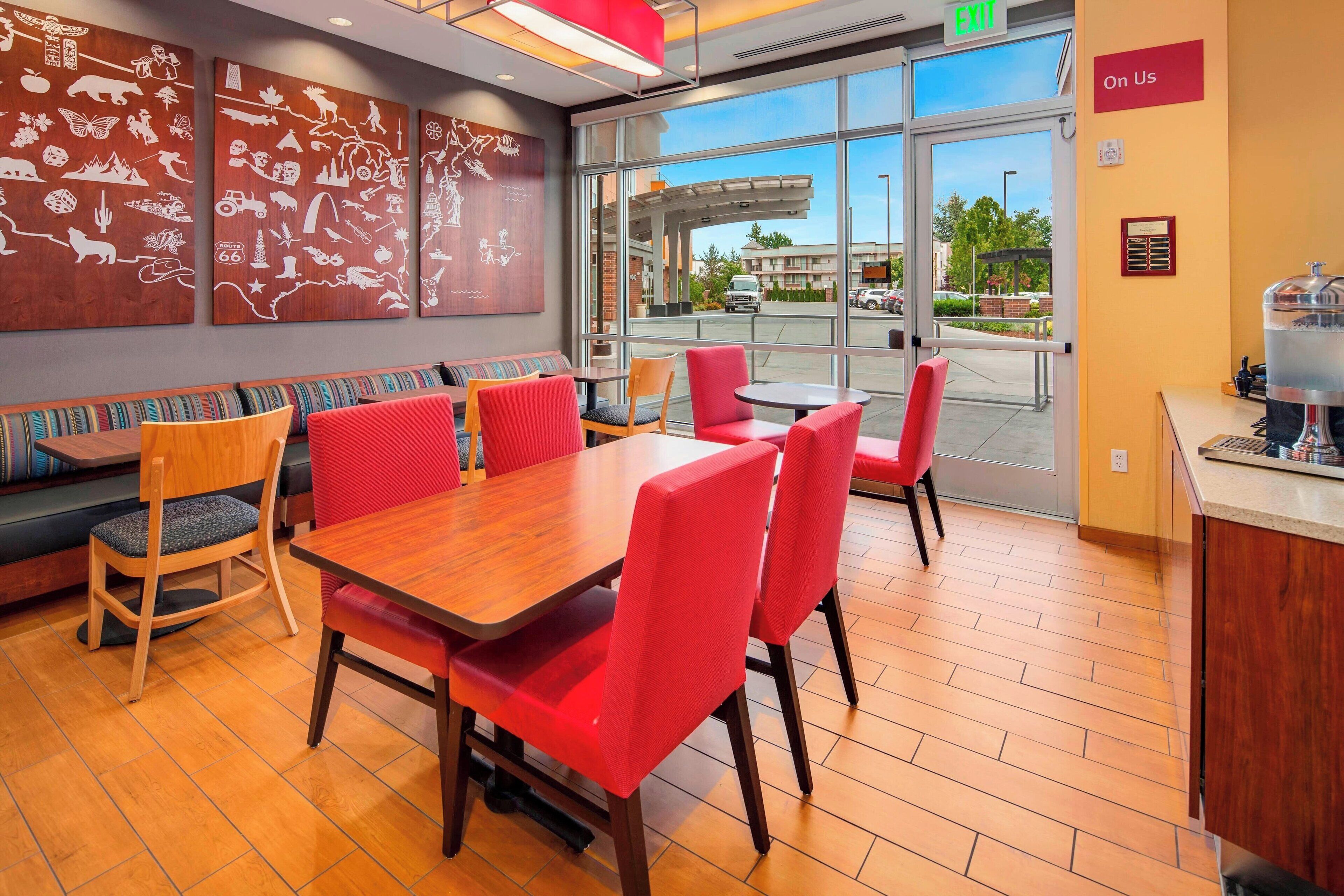 A restaurant with a wooden table and red chairs, a bench with striped cushions, and a wall with white drawings.