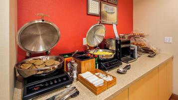 A buffet setup with various food items and cooking appliances.
