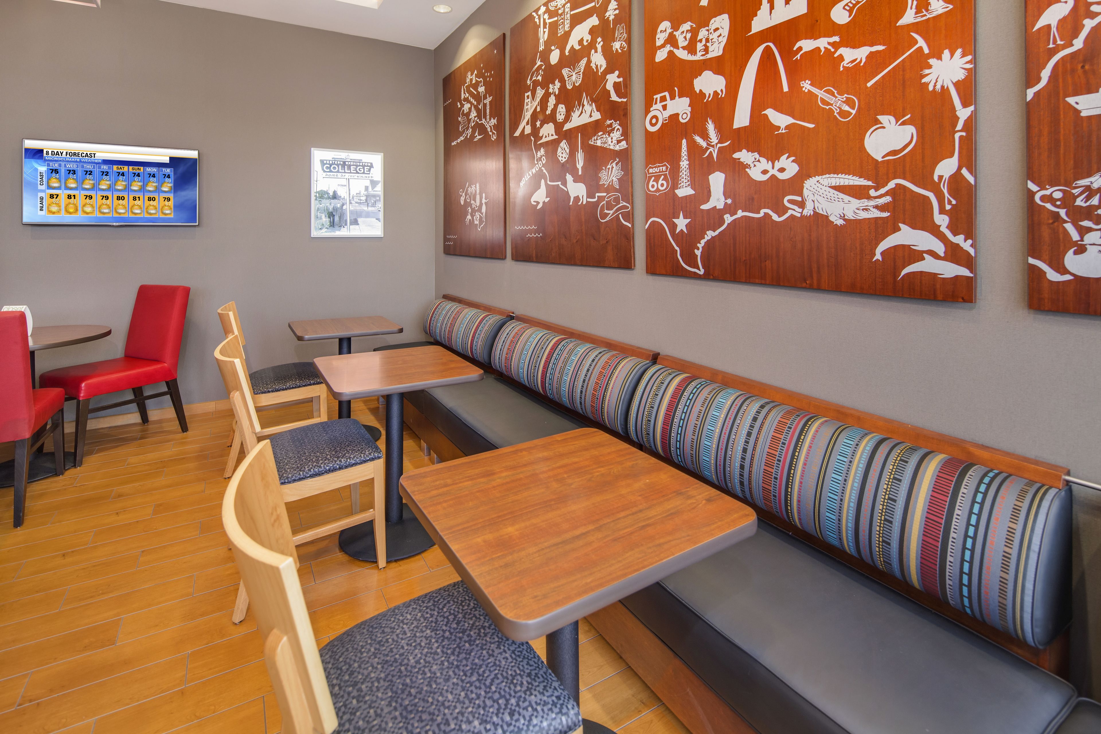 Un restaurant avec des tables et des bancs en bois, un écran affichant les prévisions météorologiques pour les neuf jours à venir, et des œuvres d’art murales représentant divers animaux et scènes.