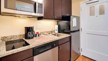 A modern kitchen with dark wooden cabinets, a stainless steel refrigerator, a built-in microwave, and a dishwasher.