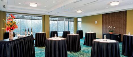 A conference room with round tables, a large window, and a carpeted floor.