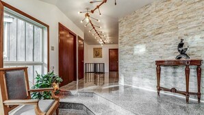 A spacious lobby with a polished stone floor, a wooden reception desk, a potted plant, and a unique wall-mounted light fixture.