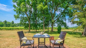 A wooden deck with a table set for two, surrounded by chairs, overlooking a vineyard.