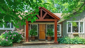 A wooden house with a porch, large windows, and potted plants.