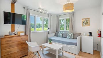 A modern, well-lit room with a wooden dresser, a white sofa with patterned cushions, a small table with a plant, and a white refrigerator.
