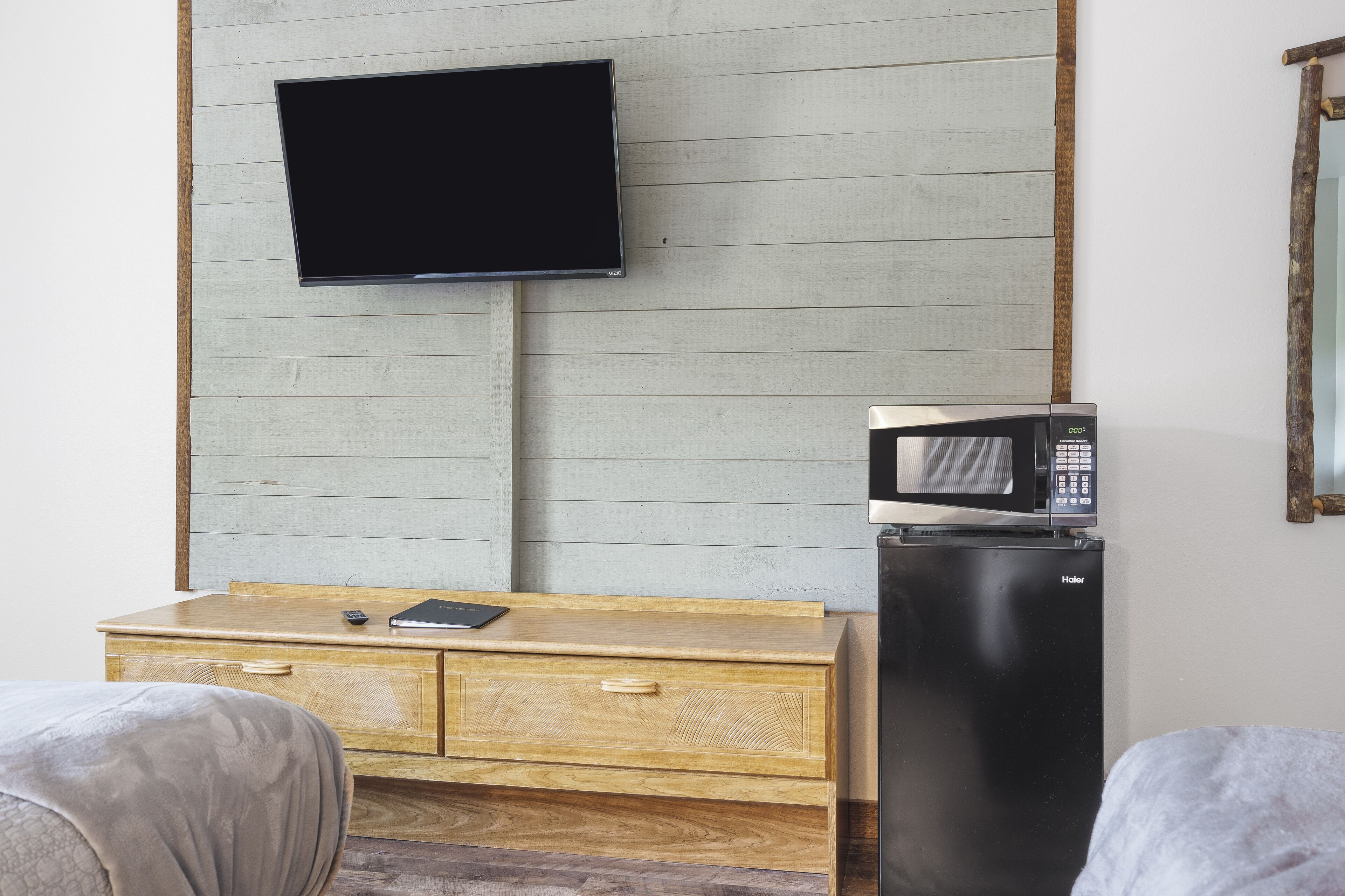 Una habitación con un aparador de madera, un televisor de pantalla plana en la pared y un refrigerador negro con un microondas encima.