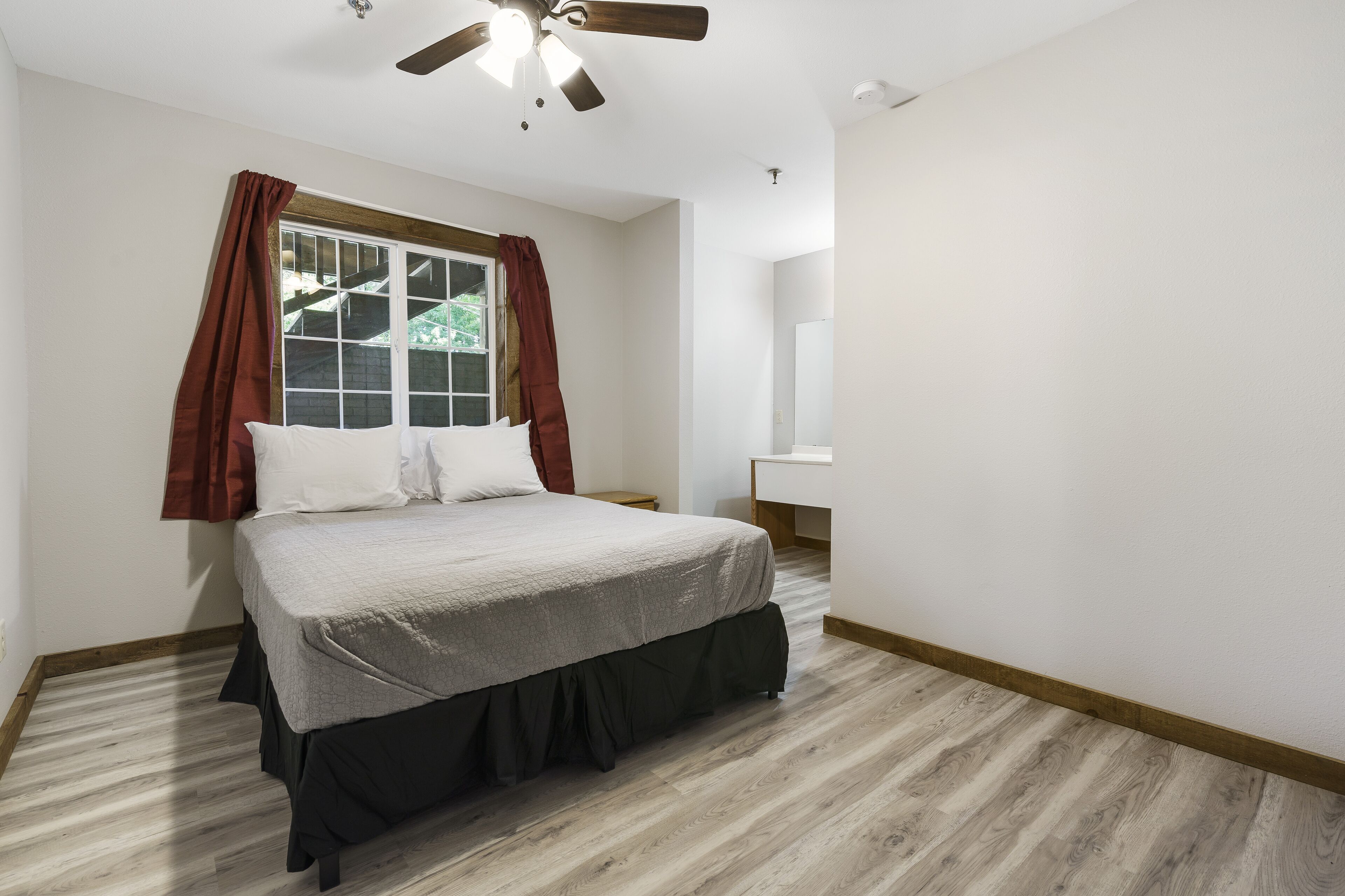 A bedroom with a bed, a window with curtains, a ceiling fan, and a nightstand.