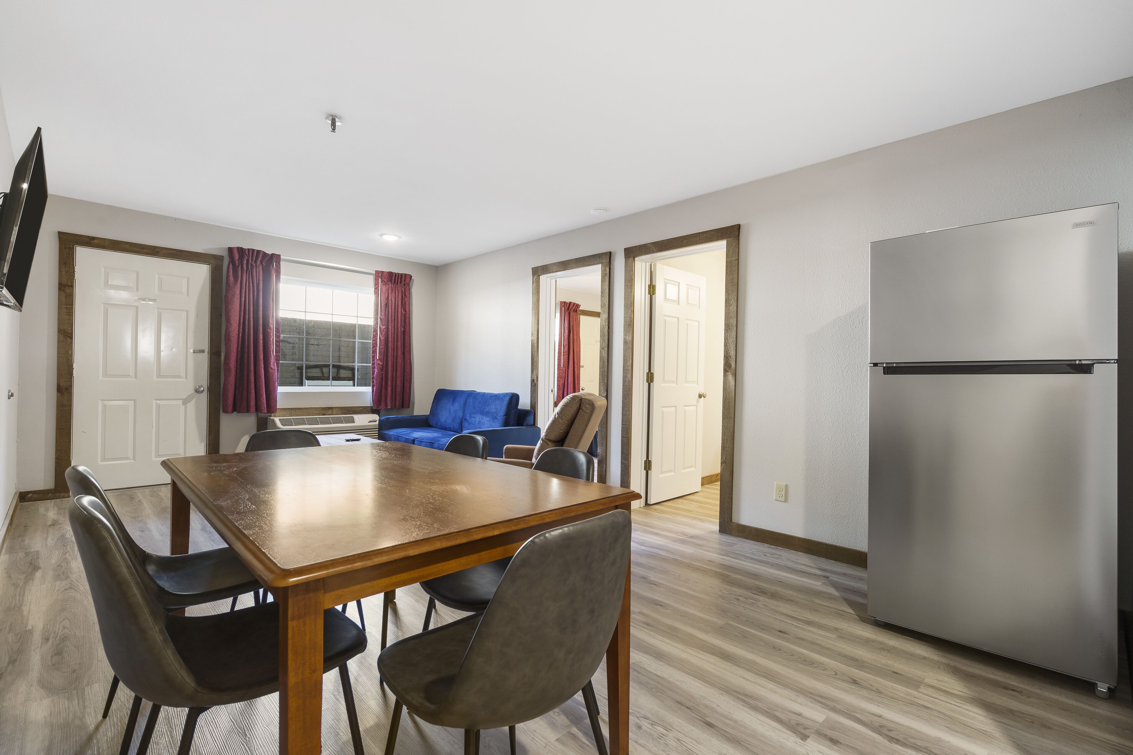 A compact living space with a dining table, chairs, a sofa, a television, and a refrigerator.