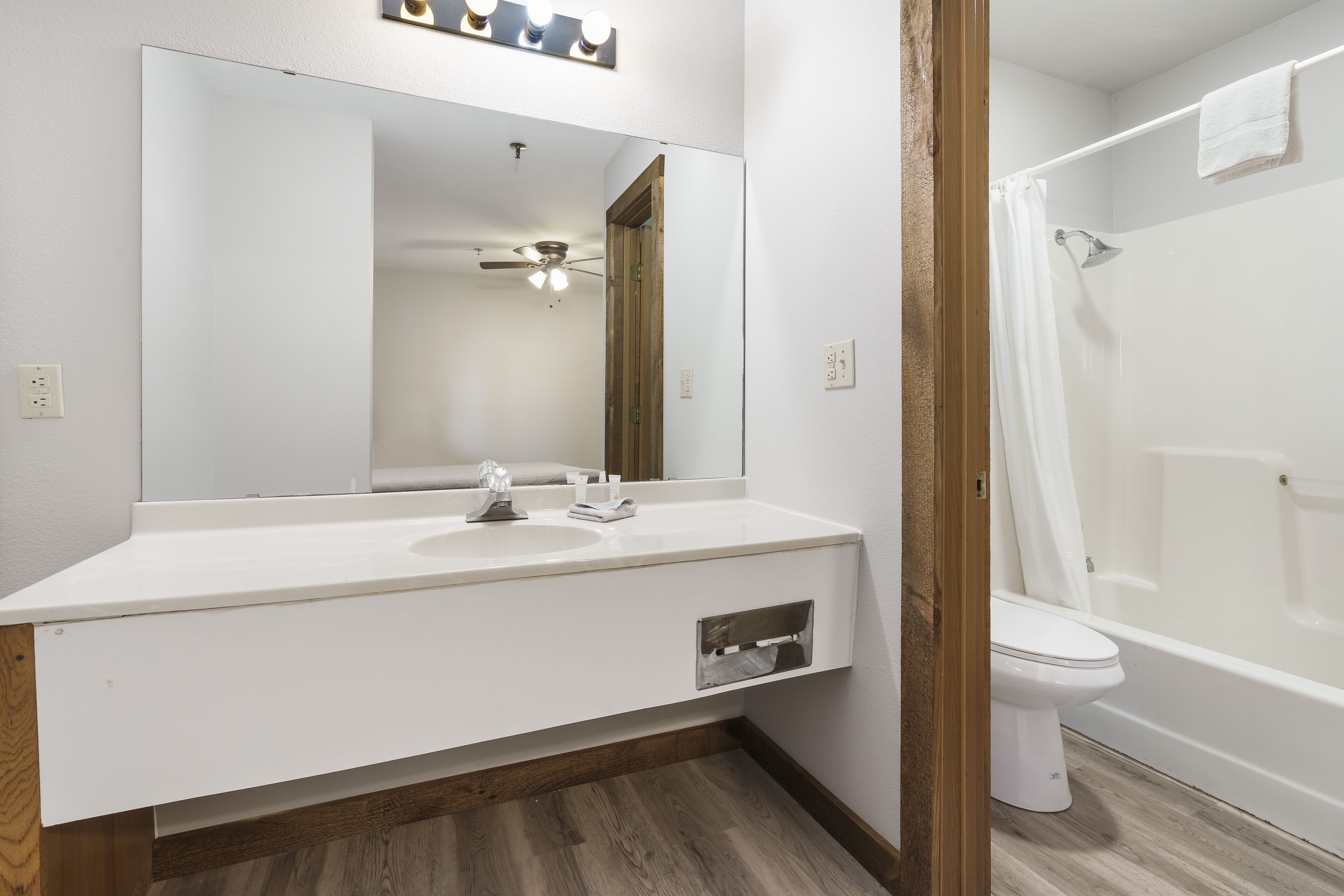 A bathroom with a white vanity, a large mirror, a ceiling fan, a shower, and a toilet.