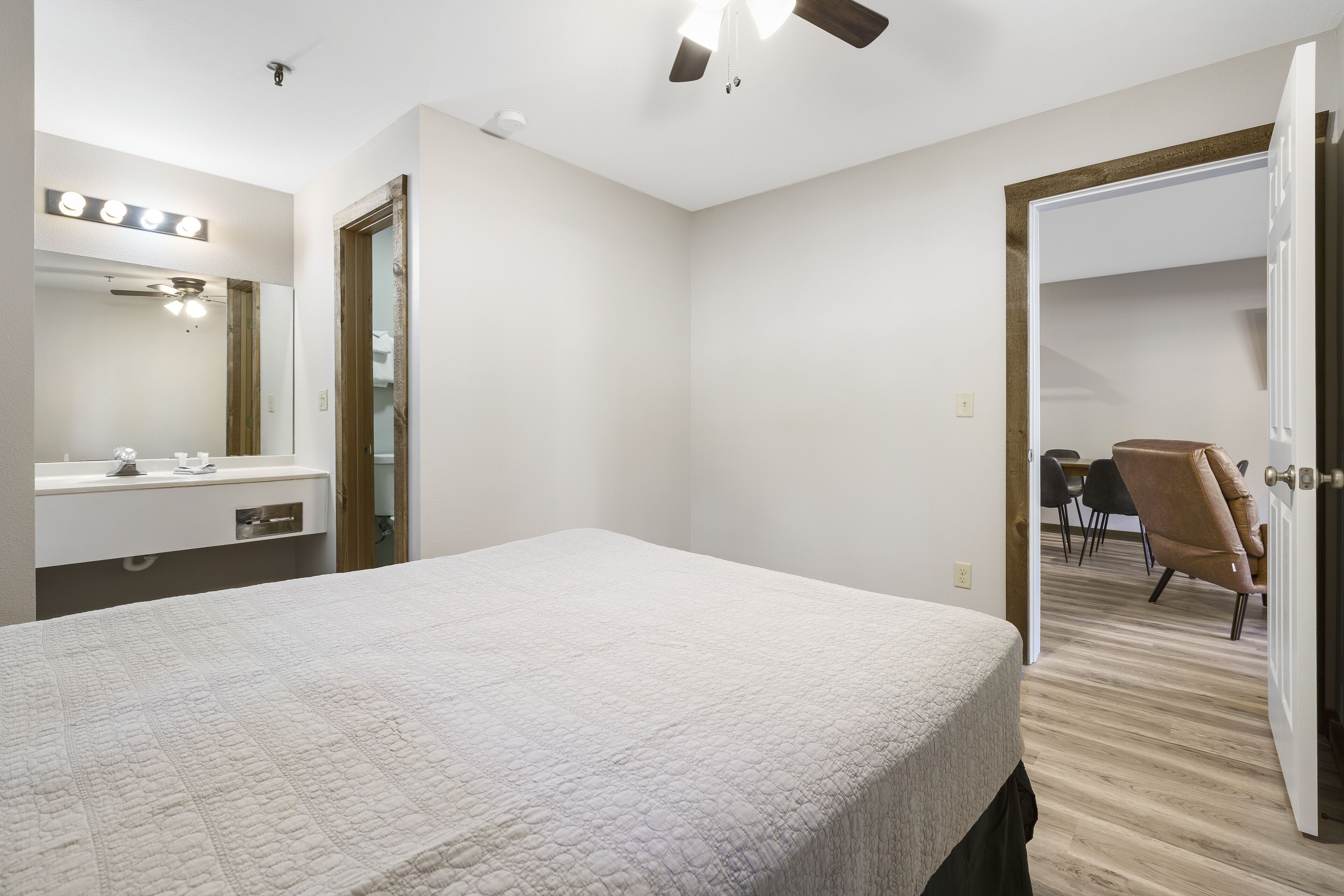 A bedroom with a bed, a vanity with a mirror, and a ceiling fan.