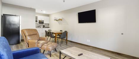 A modern living room with a blue sofa, a wooden coffee table, and a dining area with a table and chairs.