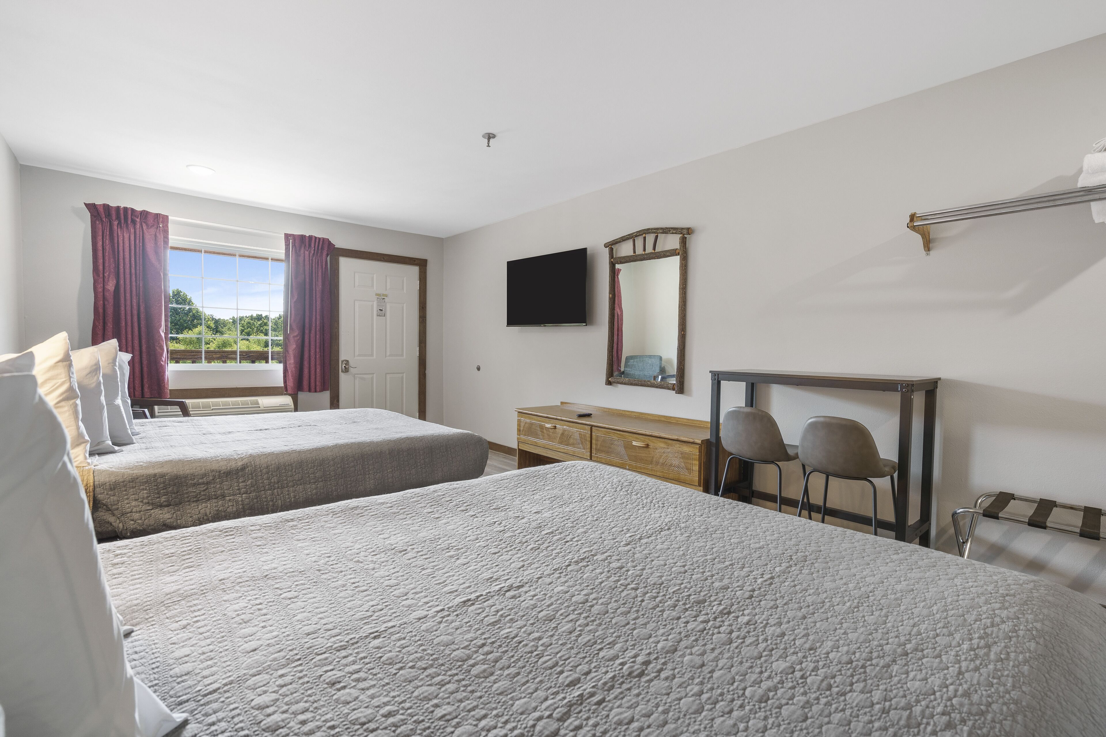 Une chambre d’hôtel avec deux lits, une télévision, une commode en bois et une fenêtre avec des rideaux.