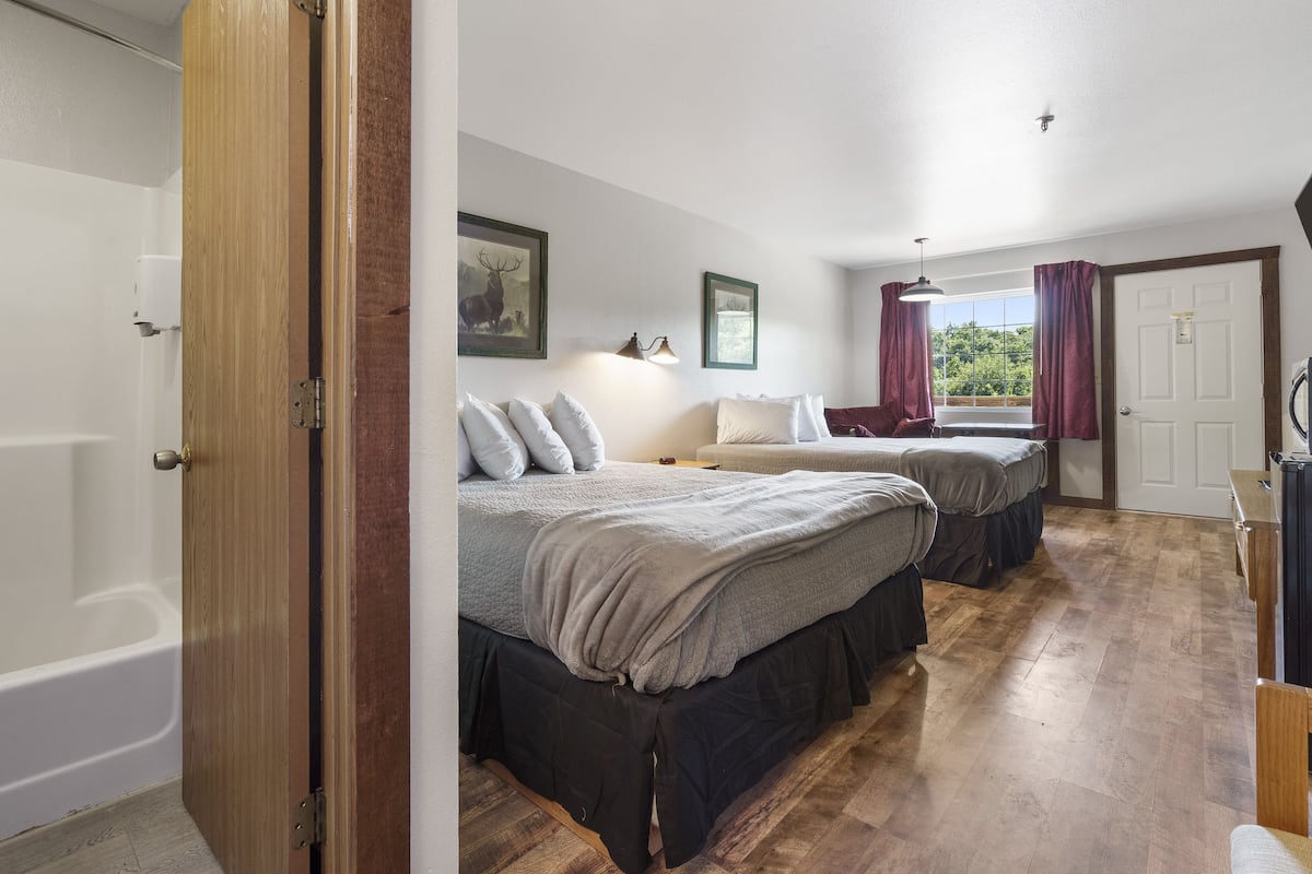Une chambre avec deux lits, un plancher en bois, une fenêtre avec des rideaux, une porte et une baignoire.