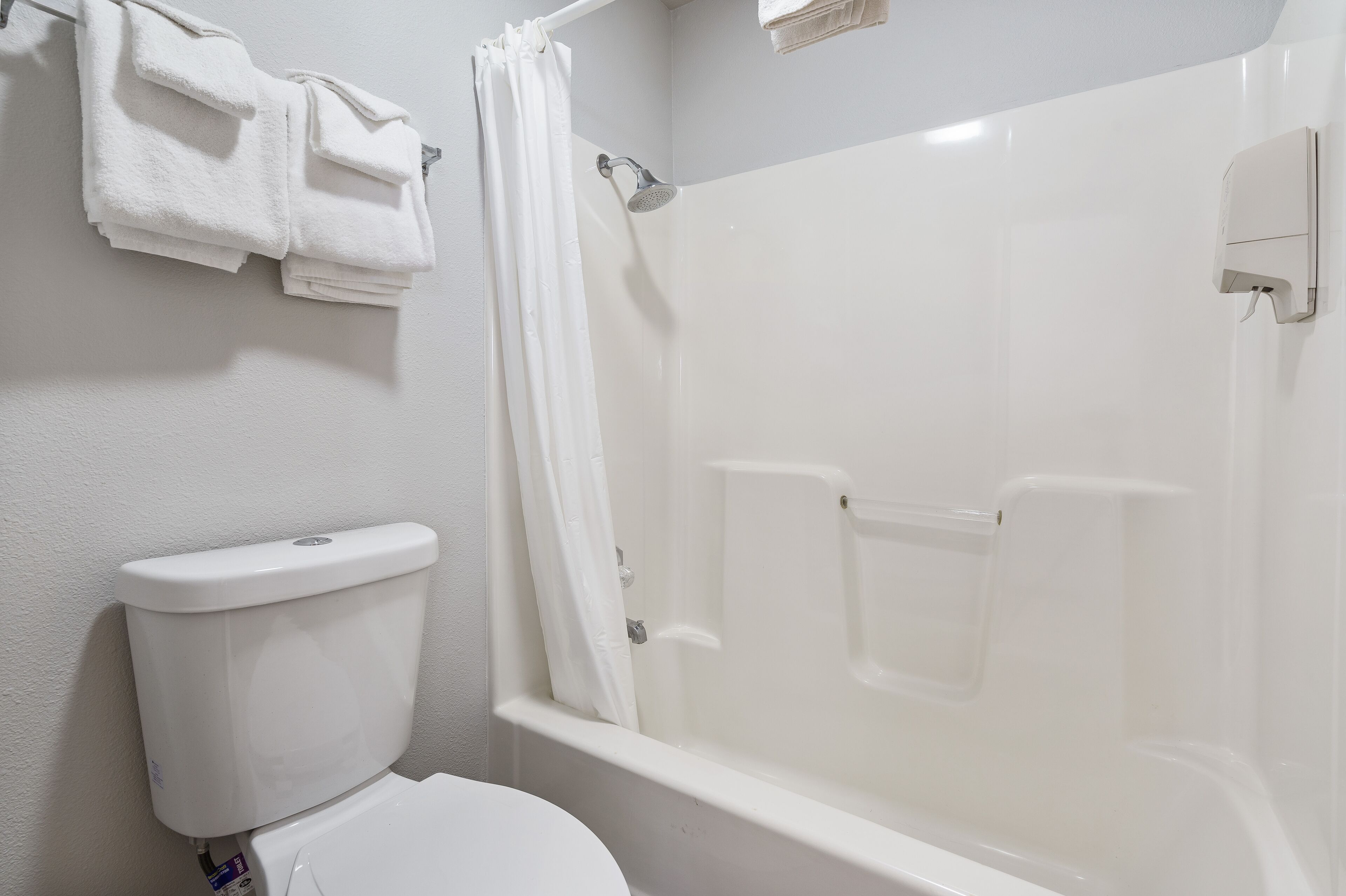A bathroom with a toilet, a shower with a glass door, and a towel rack with folded towels.