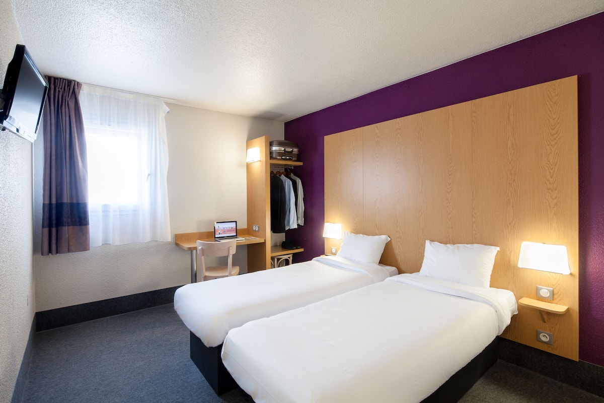 Une chambre d’hôtel avec deux lits, un bureau avec un ordinateur, une télévision et une armoire.