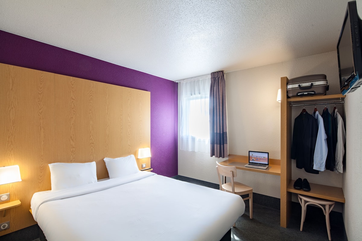 Une chambre d’hôtel avec un grand lit, un bureau avec un ordinateur portable, une armoire et une télévision.